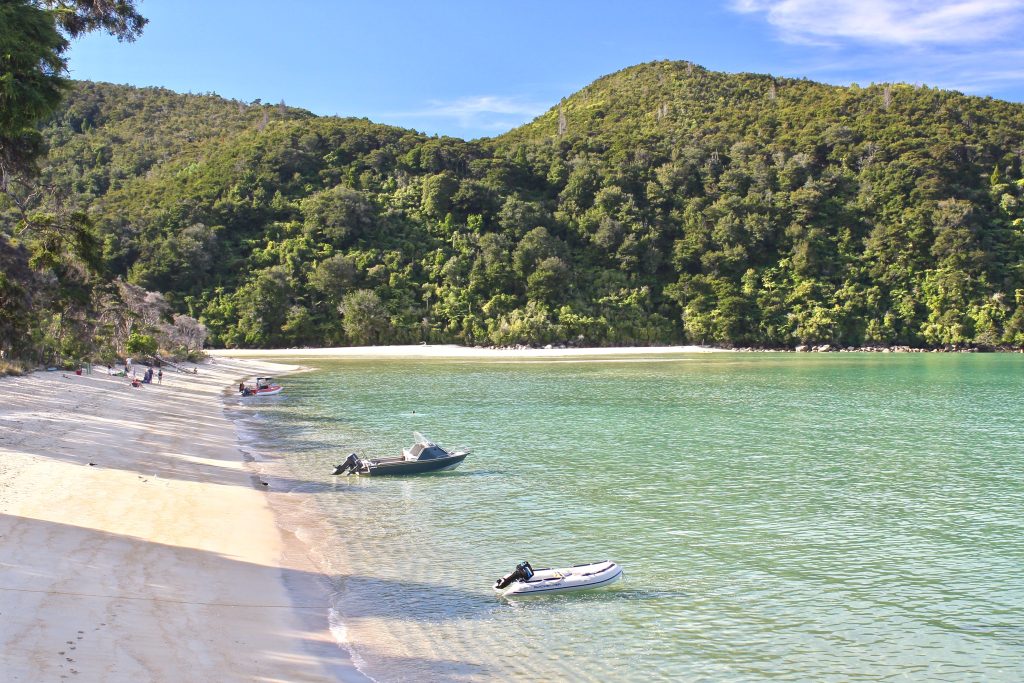 Two boats pulled up on a golden-sand beach with turquoise water in Abel Tasman National Park