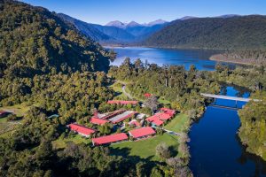 The Lake Moeraki Wilderness Lodge nestled among lush green rainforest with mountains in the distance