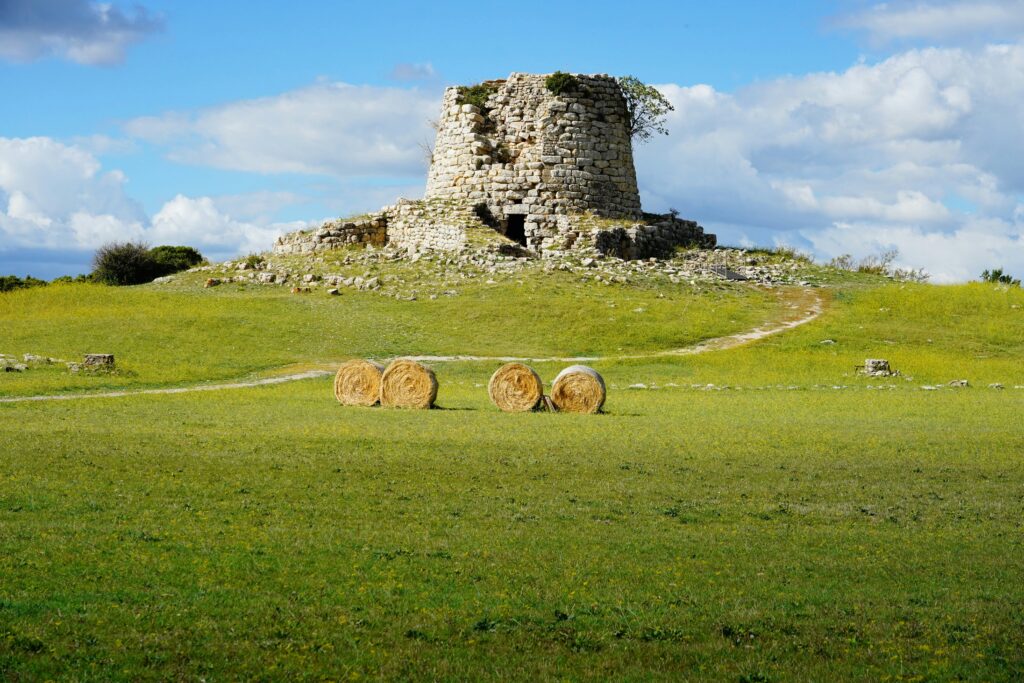 An ancient ruin atop a green hill, with hay bales in the midground