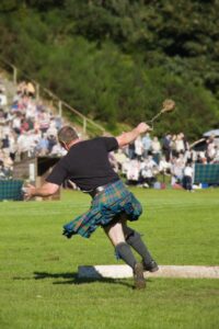 Male athlete wearing a kilt in mid-swing during the Scottish hammer throw at a Highland Games competition.