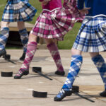 Close-up of Highland dancers performing in colorful kilts and argyle socks during a traditional Scottish Highland Games dance competition.