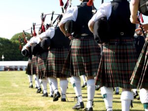 Pipe band dressed in traditional kilts marching across a grassy field at a Scottish Highland Games gathering.